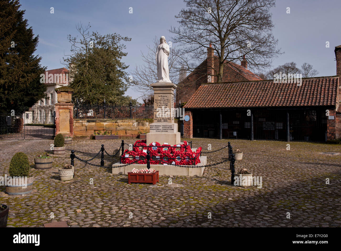Red poppy wreaths laid at base of war memorial in centre of attractive rural town - cobbled Hall Square, Boroughbridge, North Yorkshire, England, UK. Stock Photo
