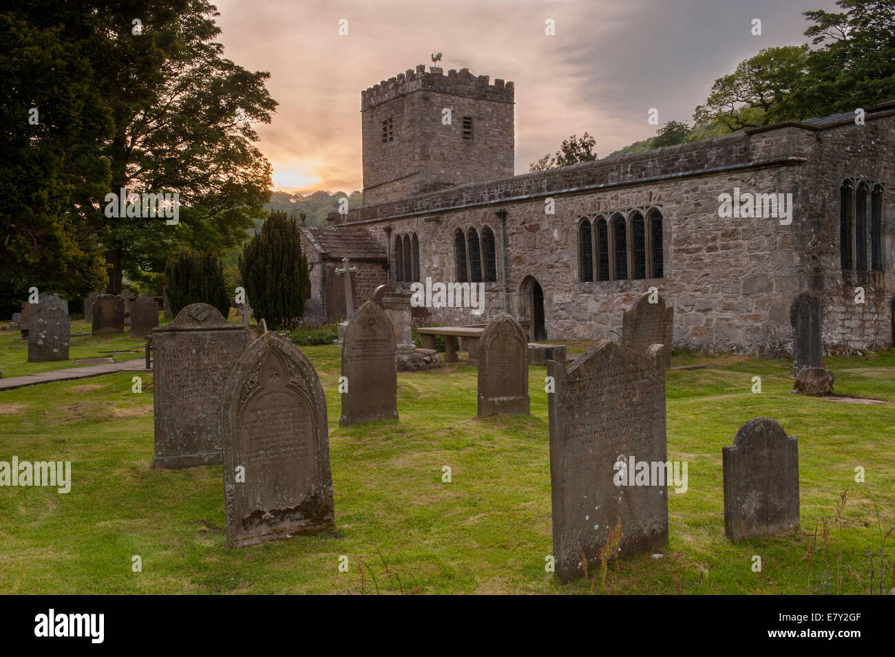 Exterior of St Michael and All Angels Church with headstones in churchyard under colourful sky at sunset - Hubberholme, Yorkshire Dales, England, UK. Stock Photo