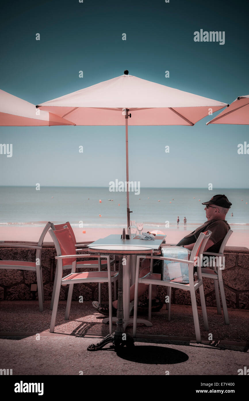 One man sitting under umbrella at cafe table by beach instagram treatment. Stock Photo