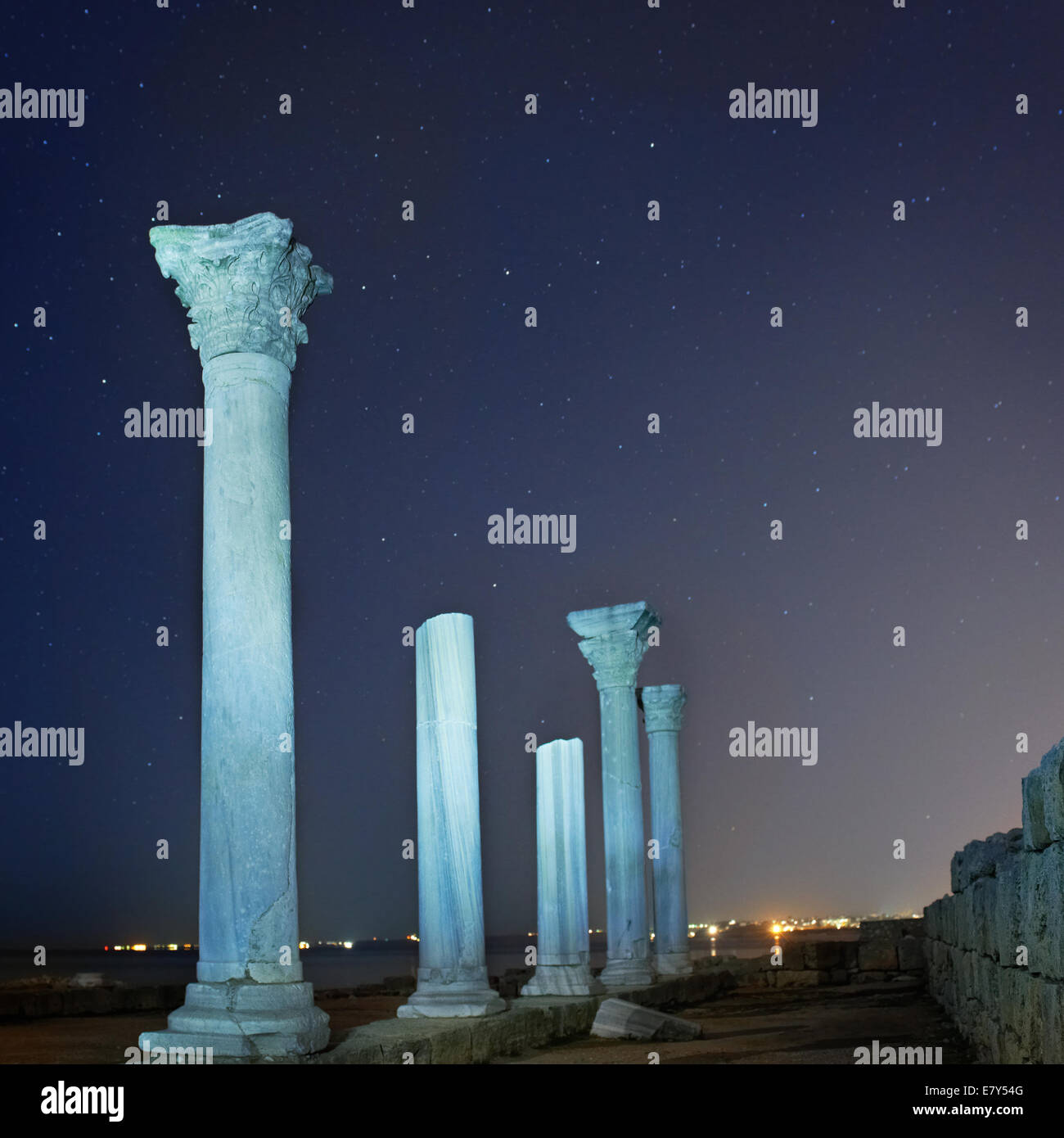 Ruins of ancient city columns under blue night sky with moon and stars ...