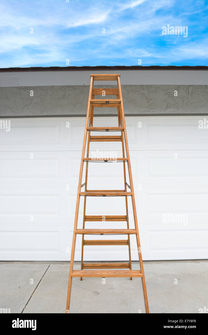 A tall wooden step ladder is positioned in from of a home's garage for a home inspector to view the roof. Composed so the sky ca Stock Photo