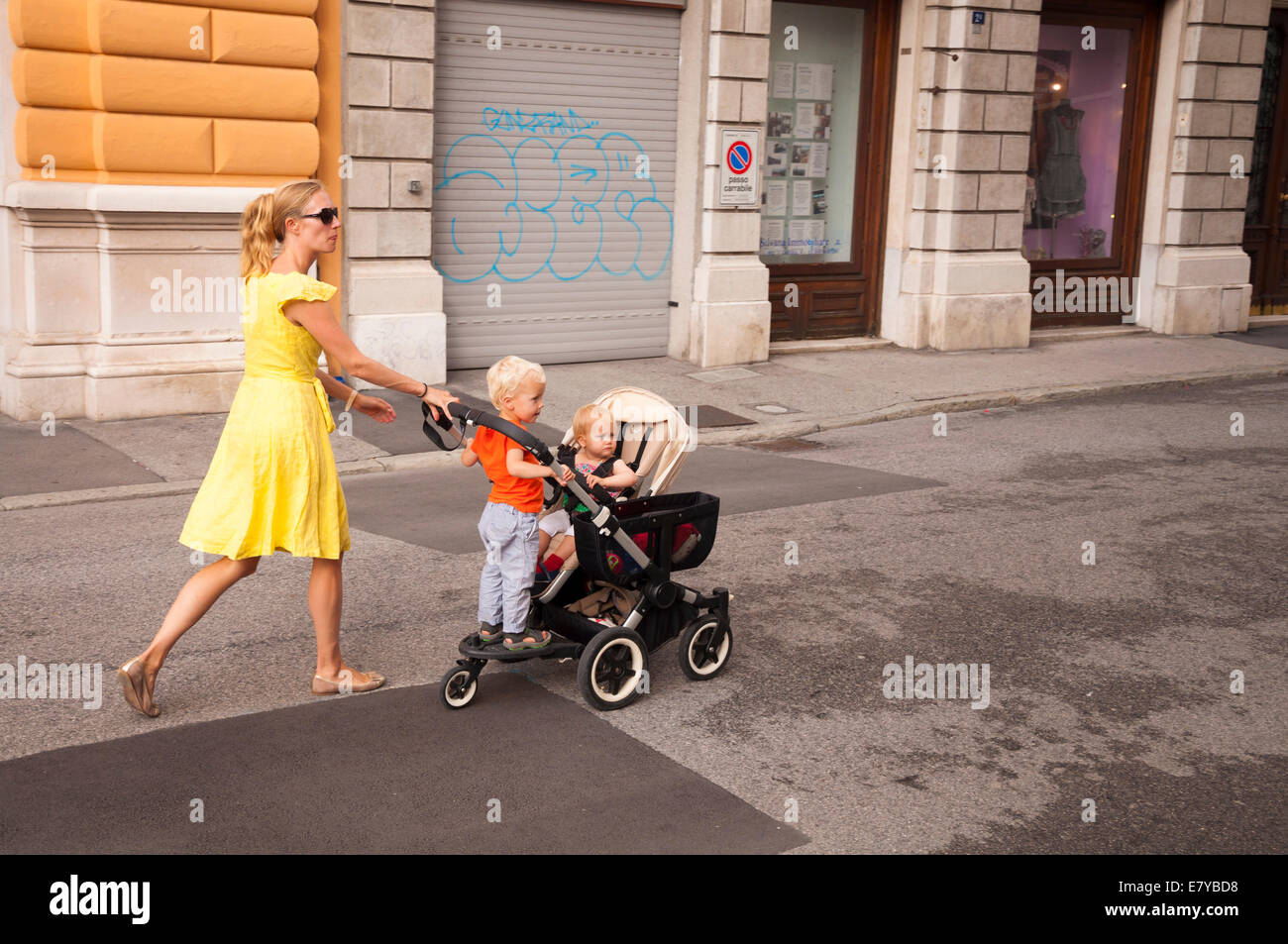 Woman walks with children in a pushchair in street in Trieste Italy Stock Photo
