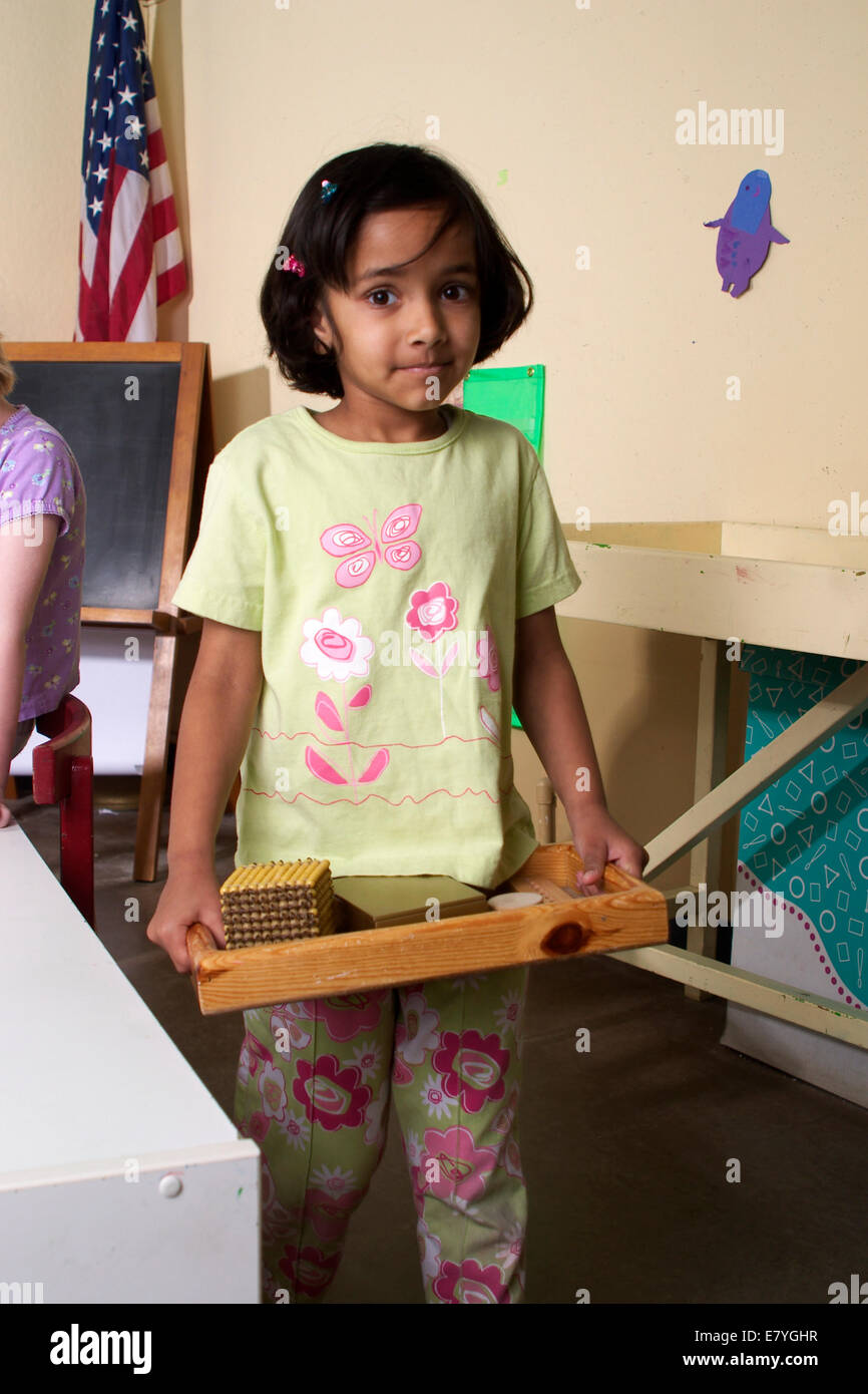 4-5 year old students student girl girls carries Indian heritage carries project tray in classroom  eye contact MR © Myrleen Pearson Stock Photo