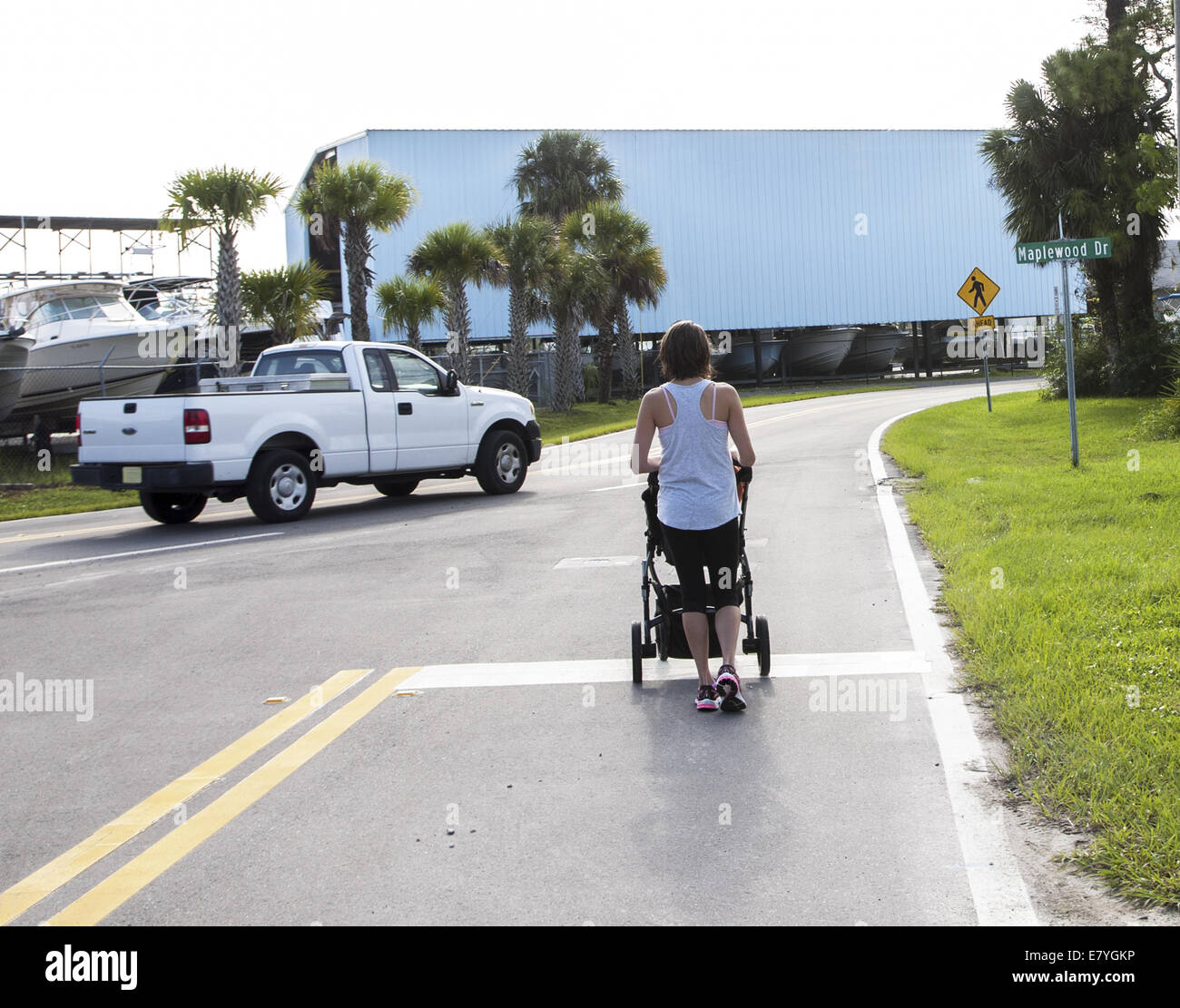 Lady pushing a stroller stopped at stop mark on road waiting for a pick up truck to go by. Stock Photo