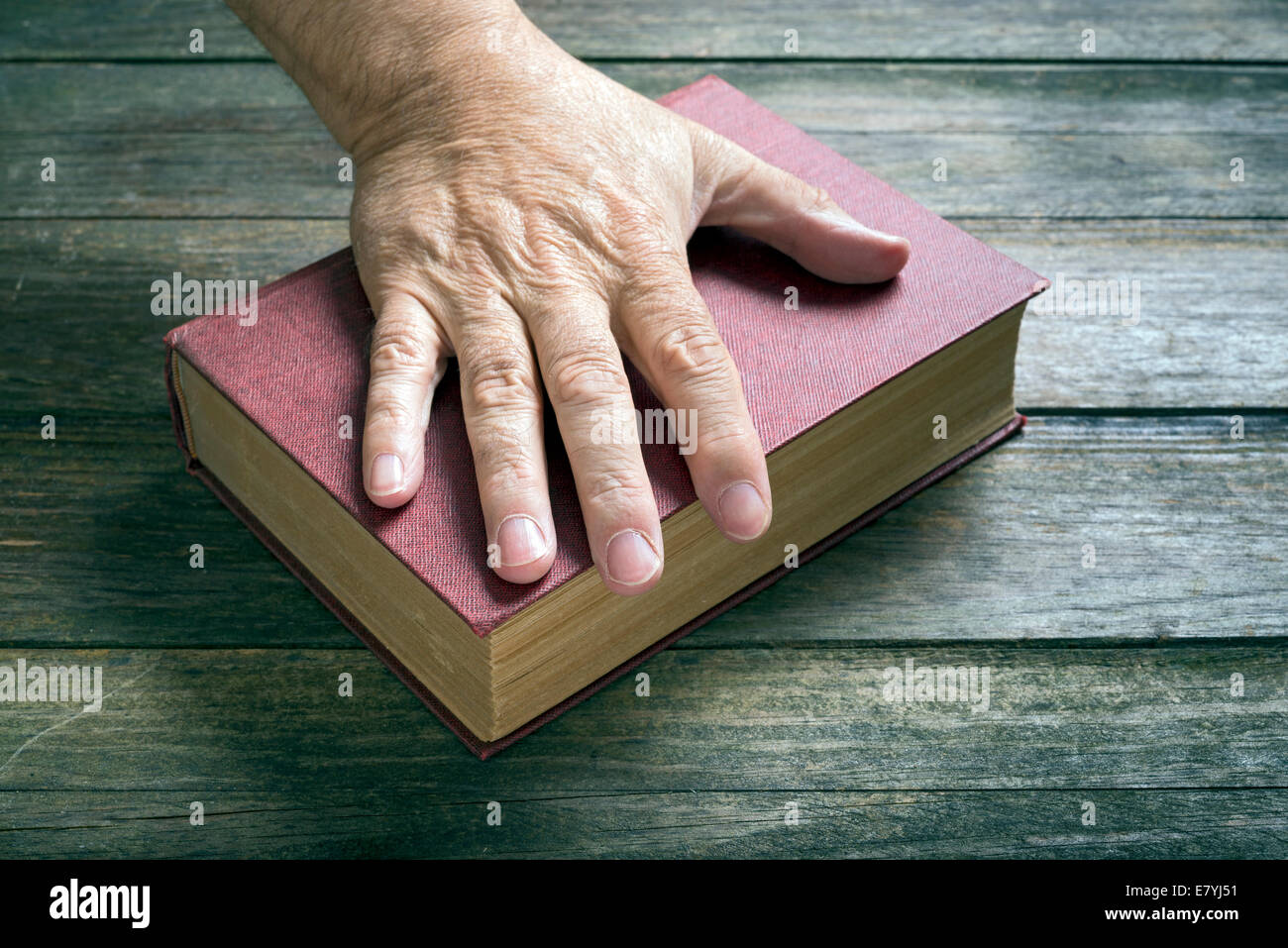 A man is resting his left hand on a red book at a table Stock Photo