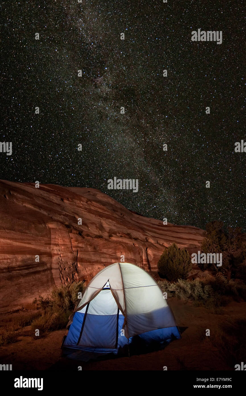 A tent is illuminated in a remote camping site while the Milky Way galaxy displays overhead. Stock Photo