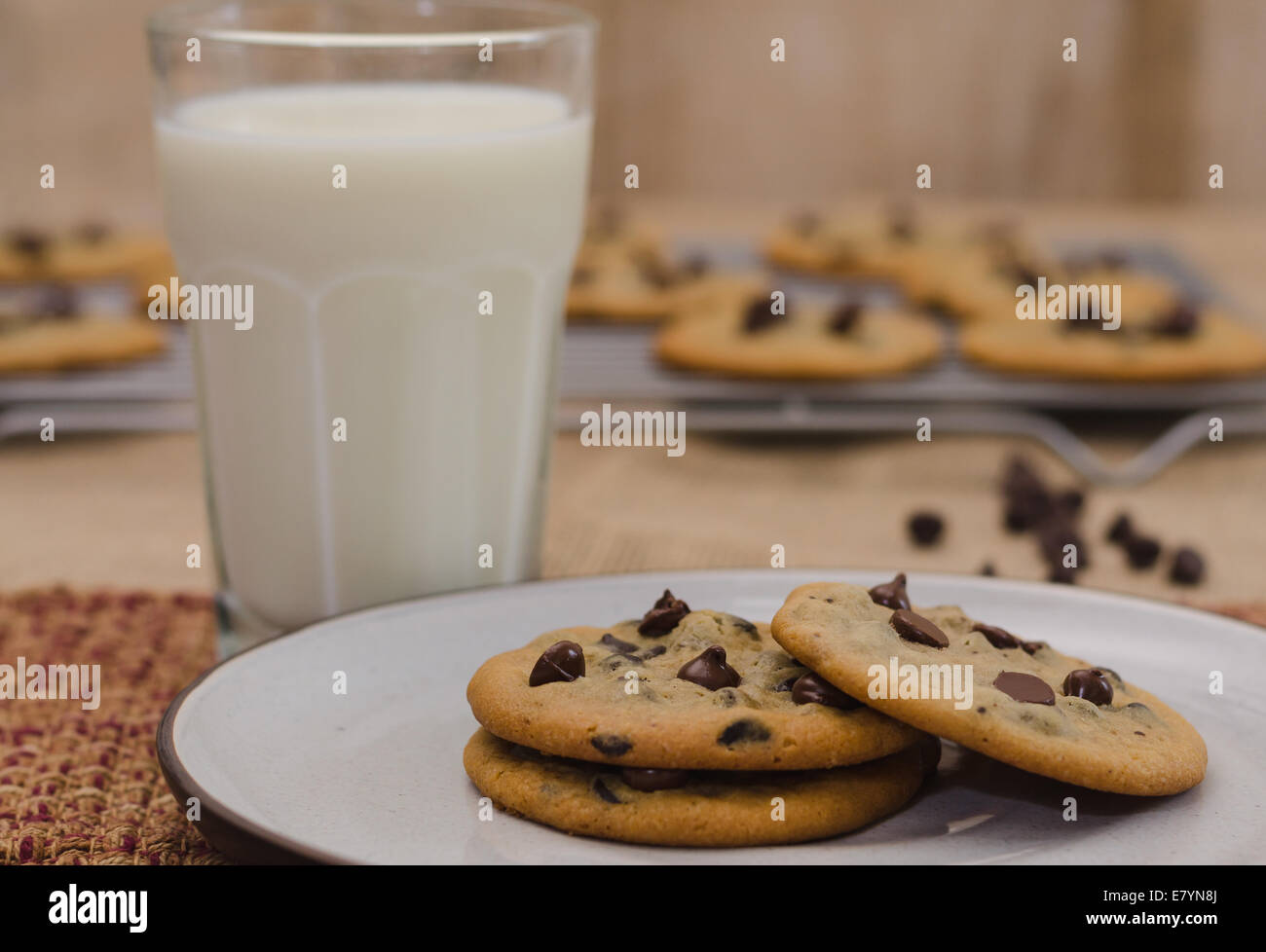Chocolate chip cookies on plate with glass of milk, and rack of cooling cookies in the background Stock Photo