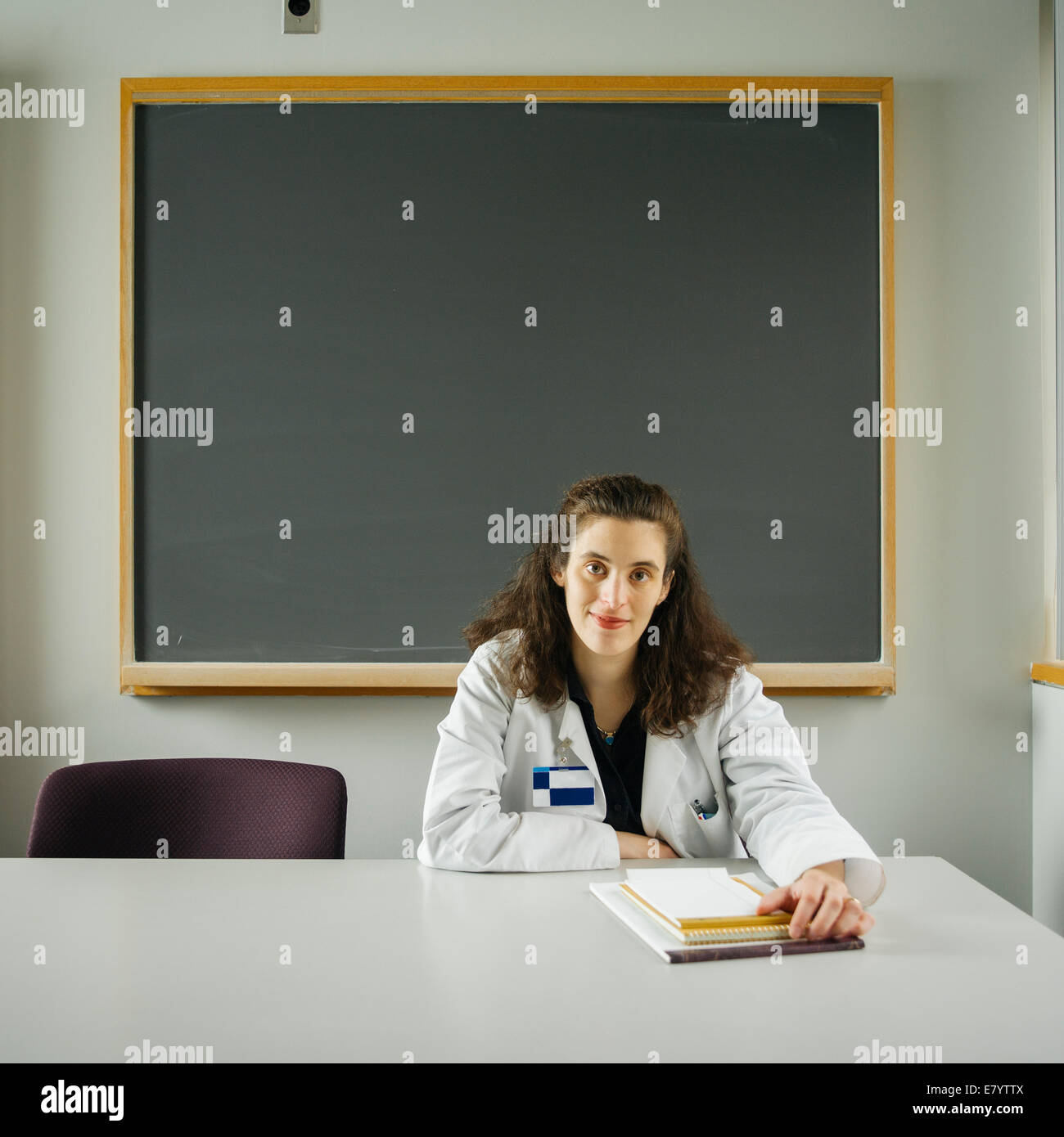 Woman at classroom desk with chalkboard in background Stock Photo