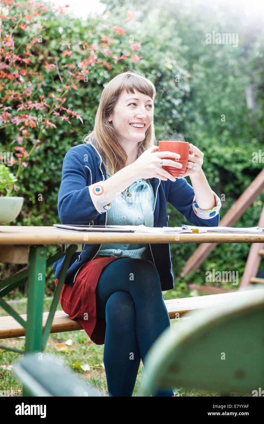 Woman sitting outdoors with tablet pc, Holding mug and smiling Stock Photo