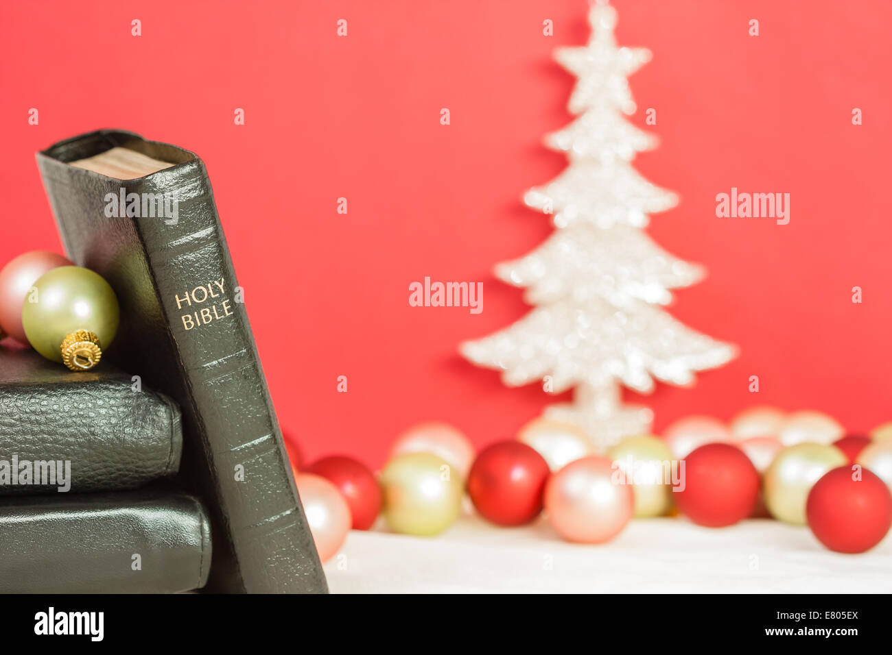 A sharply focused Holy Bible with Christmas tree and ornaments against red background. Can be used for Christmas Bible passages. Stock Photo