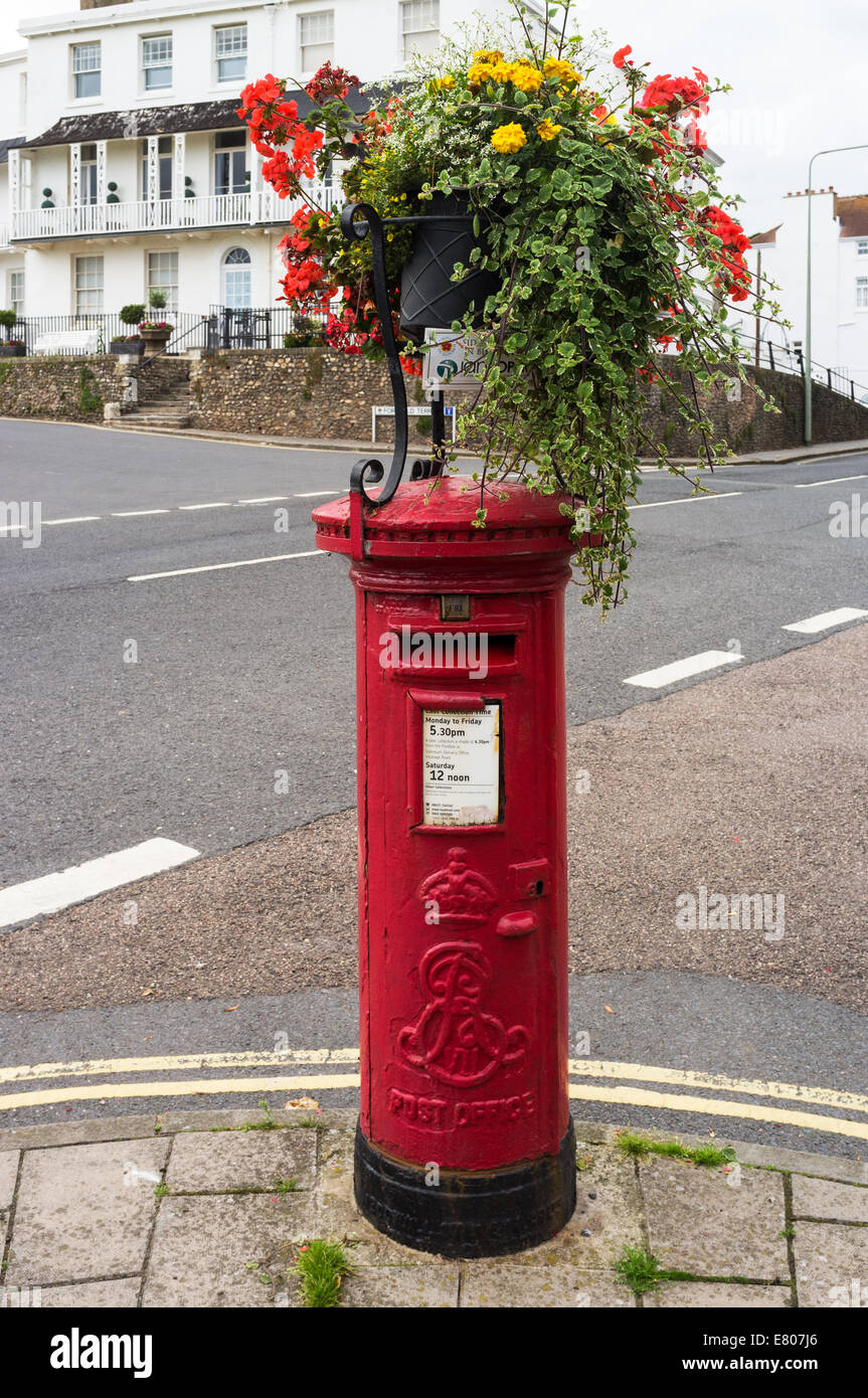 An Edwardian red pillar box in Sidmouth, Devon with a floral display mounted on it's top. Stock Photo