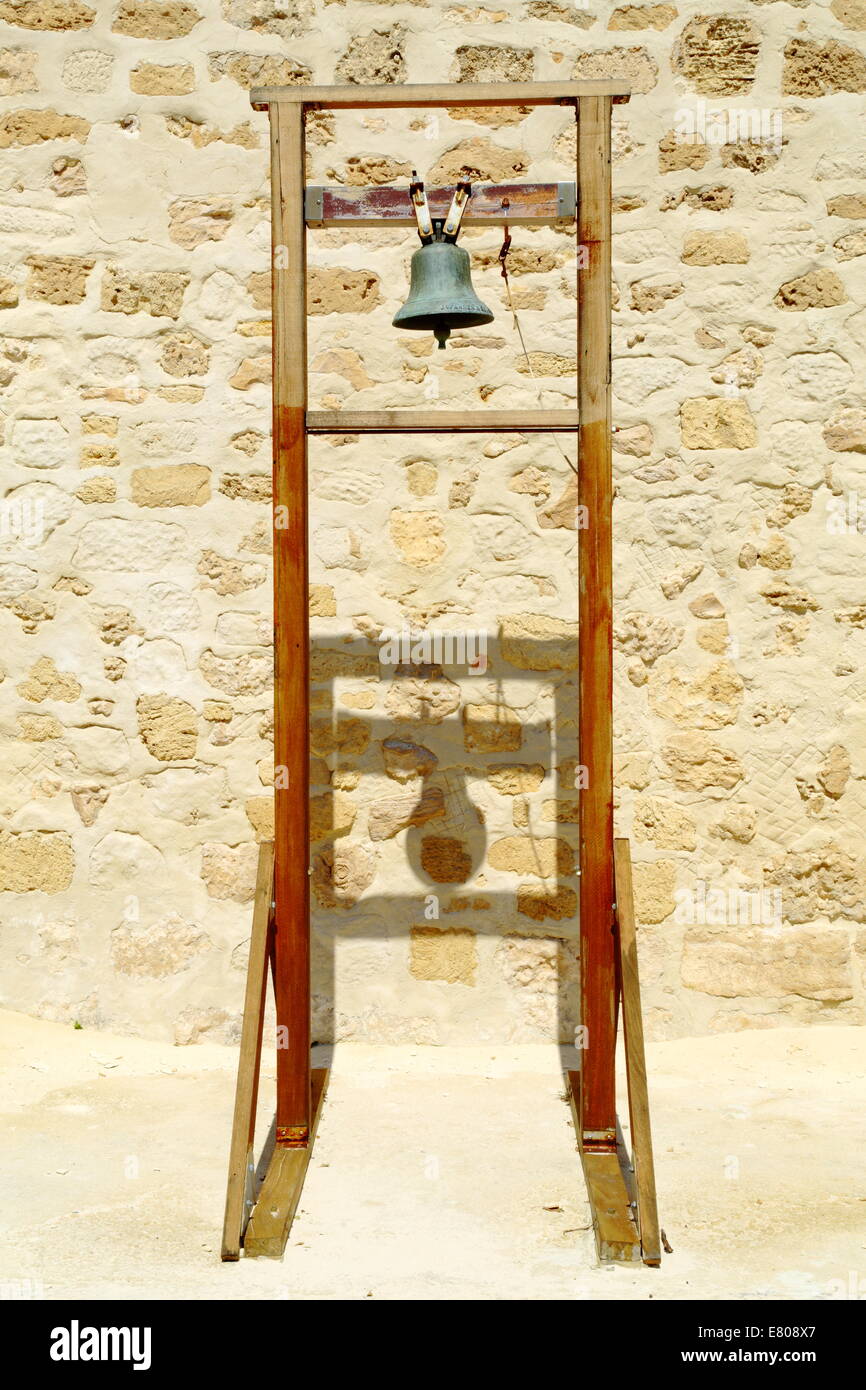 An old bell on and wooden stand cast shadows against the limestone block walls of The Roundhouse, Fremantle, Western Australia. Stock Photo