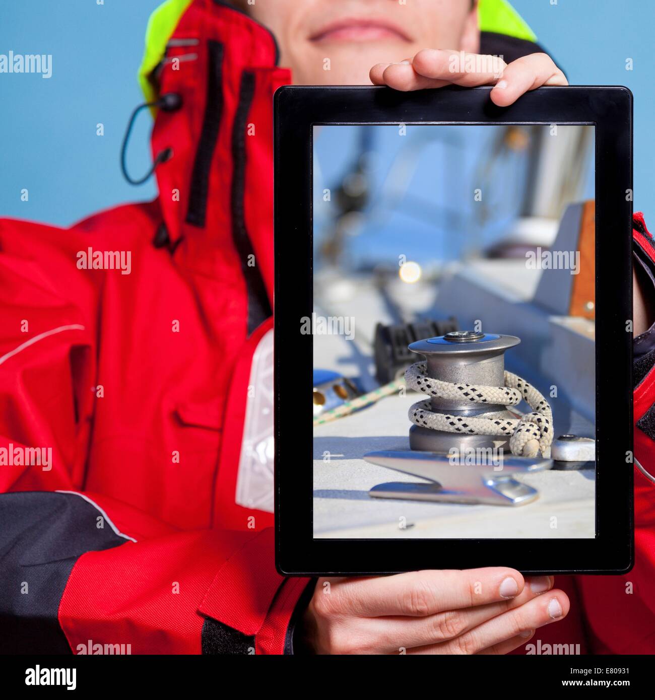 Man in wind jacket holding ipad with photo of yacht sailboat. Sailor showing screen tablet touchpad dreaming about yachting sail Stock Photo