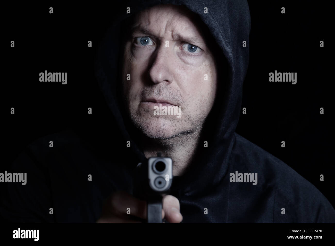Closeup front view of mature man, looking forward, with gun in hand on black background Stock Photo