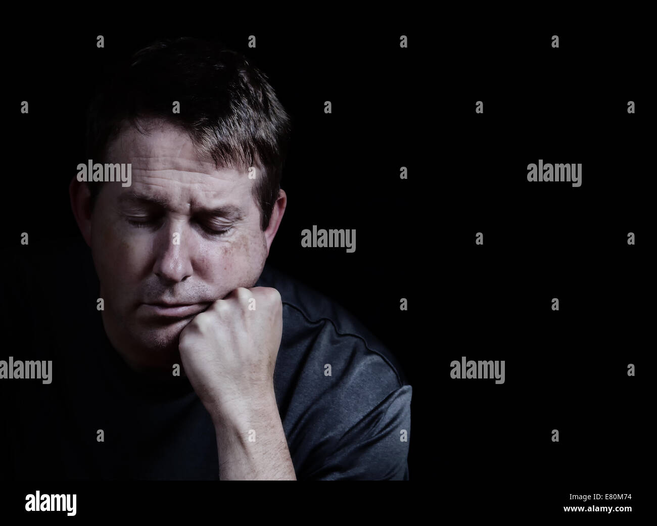 Front view close up of mature man with his eyes closed and chin in hand displaying depression on black background Stock Photo