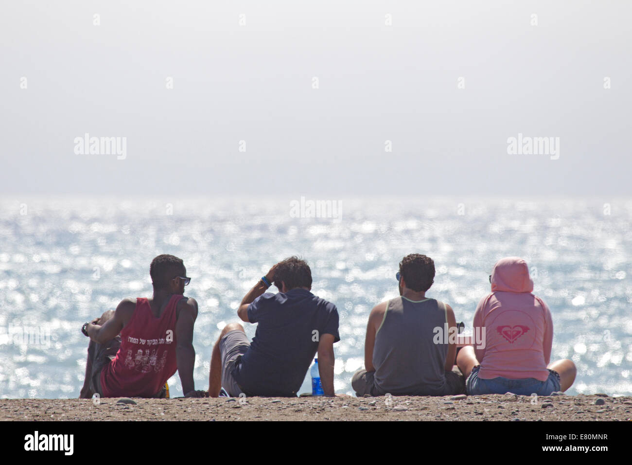 Four People Sitting on the Beach with Backs to the Camera Stock Photo