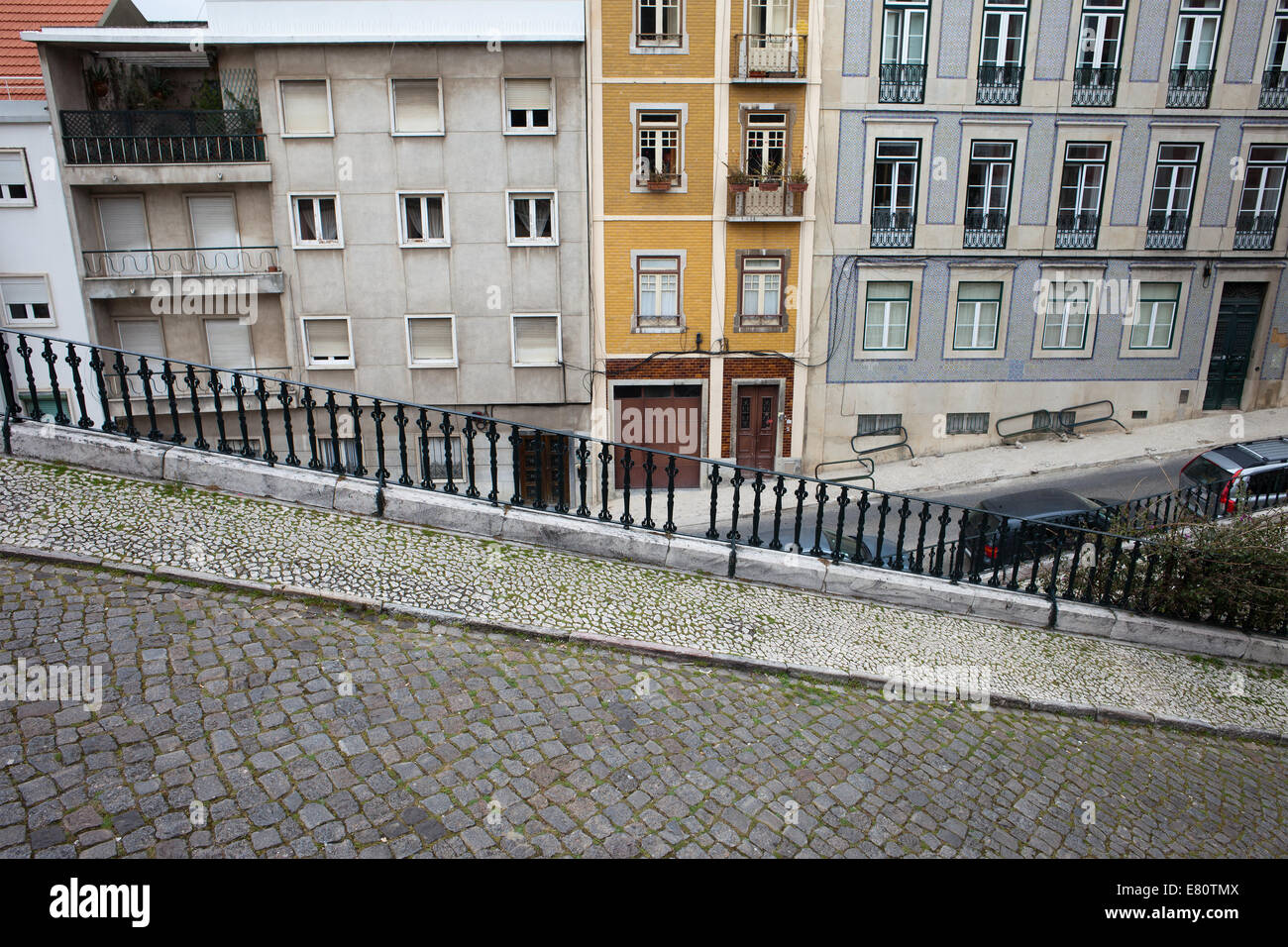 Descending, steep, cobbled street with sidewalk and houses in the background in Lisbon, Portugal. Stock Photo
