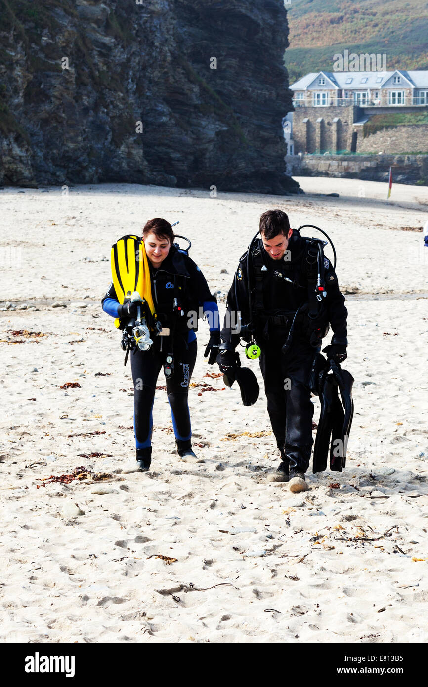 Two scuba divers diving equipment air tank tanks wet suits suit breathing apparatus walking from sea on beach divers Stock Photo