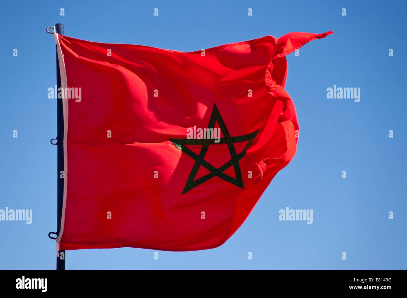 Horizontal close up of the national flag of Morocco against a blue sky. Stock Photo
