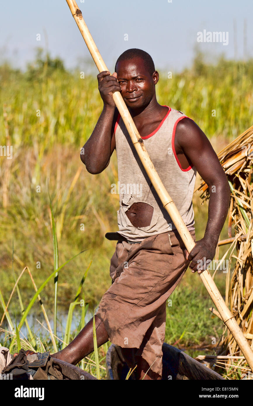 a fisherman poses with a bamboo pole used to push a dugout canoe