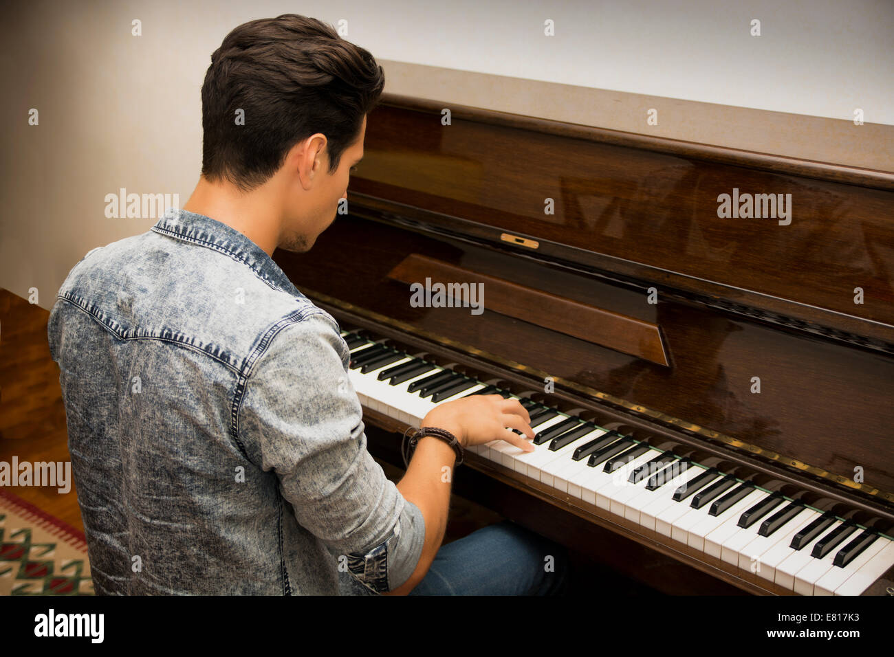 Young handsome male artist playing his wooden classical upright piano, indoor portrait Stock Photo