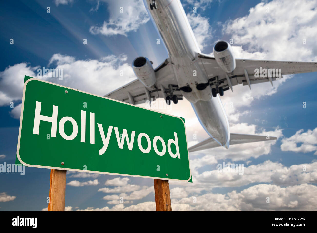 Hollywood Green Road Sign and Airplane Above with Dramatic Blue Sky and Clouds. Stock Photo