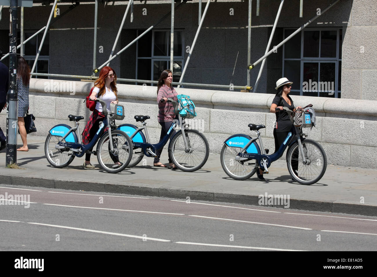 Three females walking bicycles along a pavement in London Stock Photo