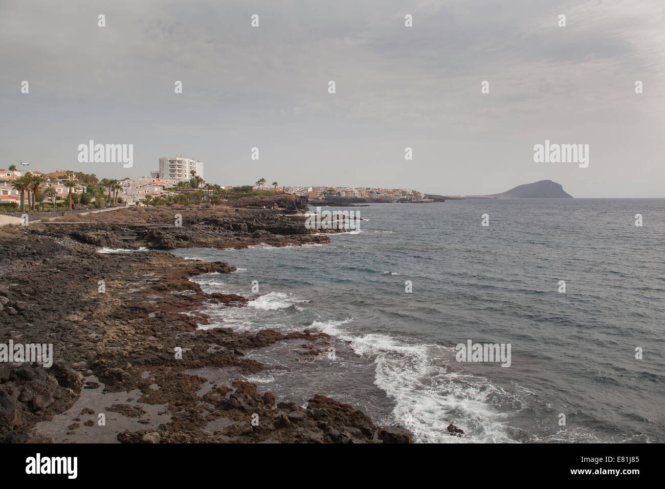 Canary Islands Tenerife rocky beach waves break town in distance Stock Photo
