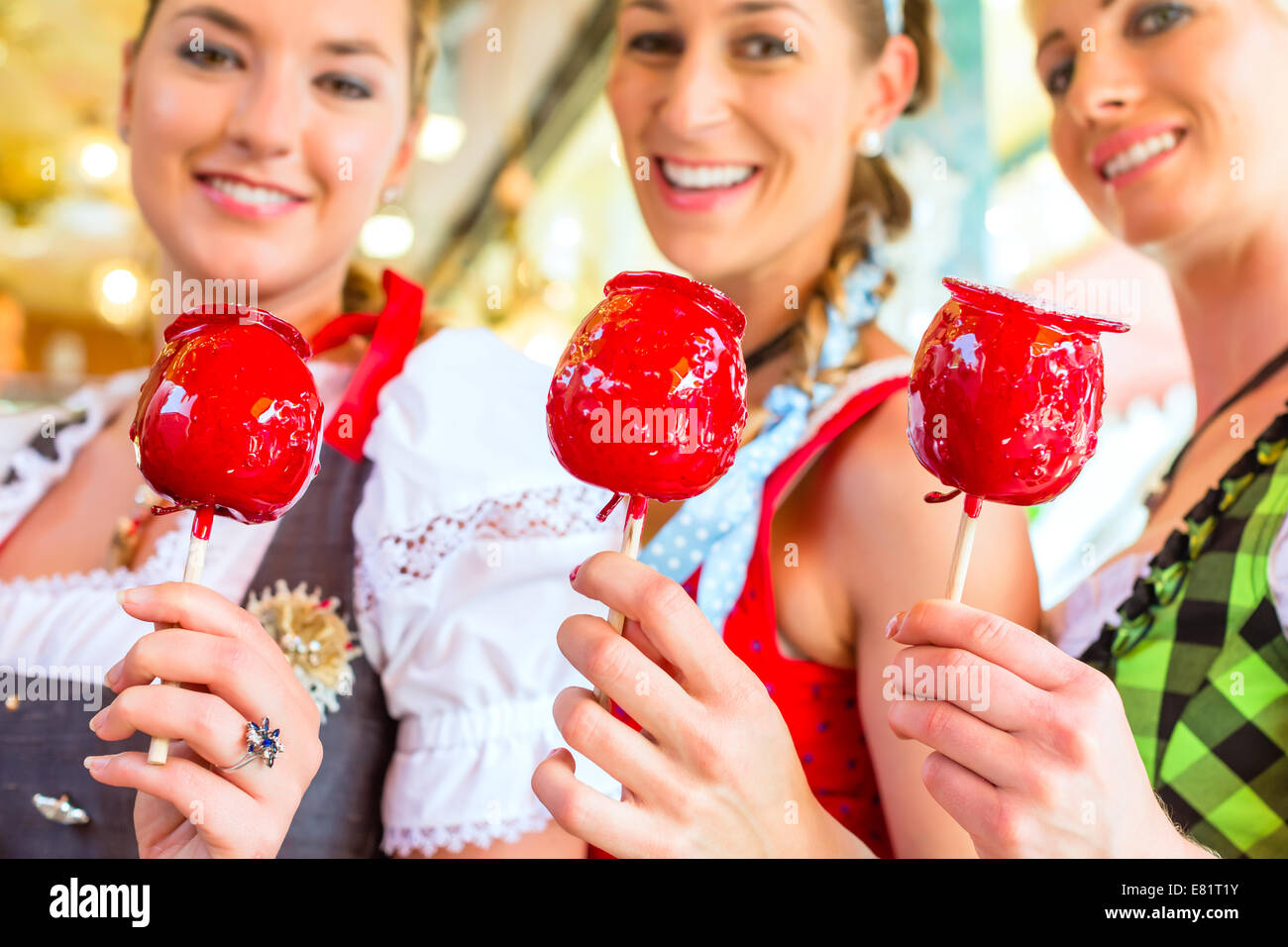 Friends visiting together Bavarian fair in national costume eating candy apple Stock Photo
