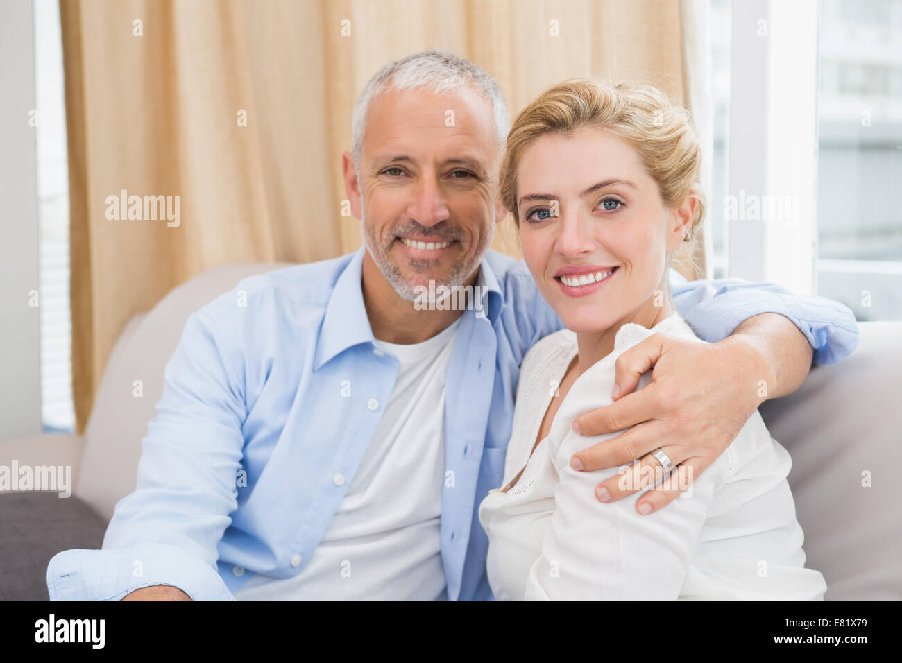 Happy couple smiling at camera on sofa Stock Photo - Alamy