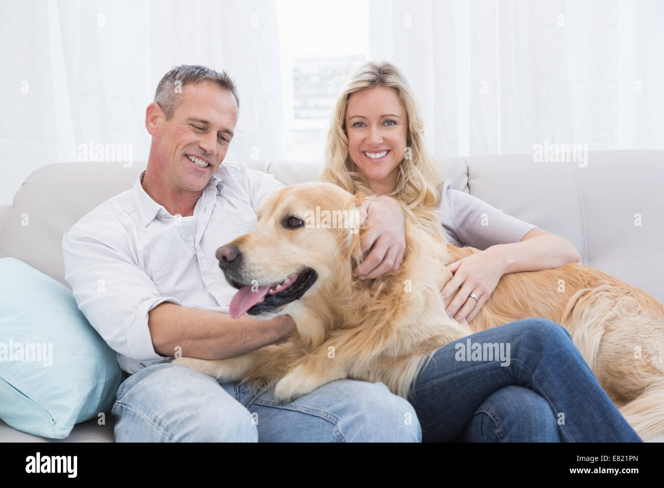 Smiling couple petting their golden retriever on the couch Stock Photo