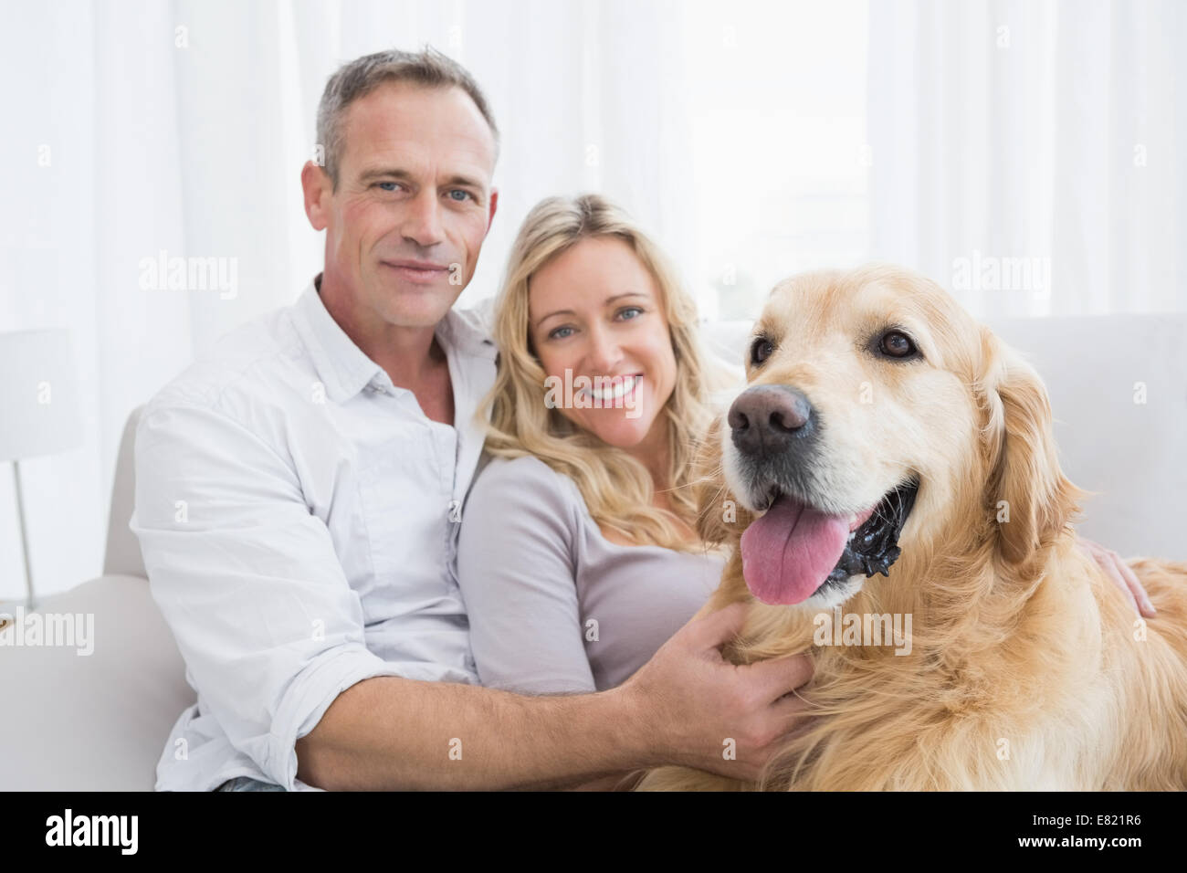 Smiling couple petting their golden retriever on the couch Stock Photo