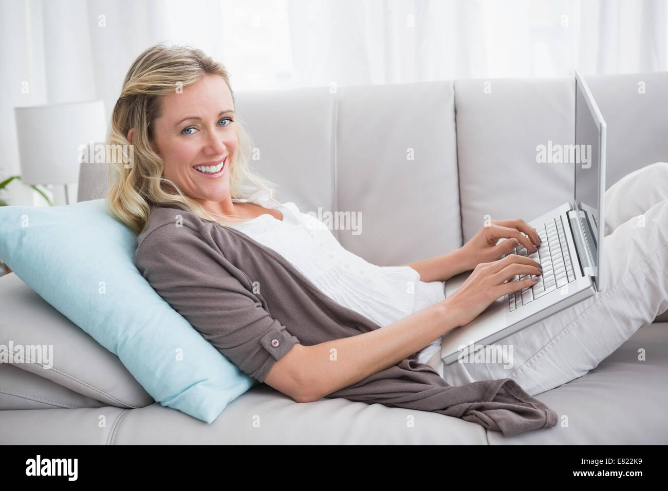 Woman lying on sofa using her laptop smiling at camera Stock Photo - Alamy
