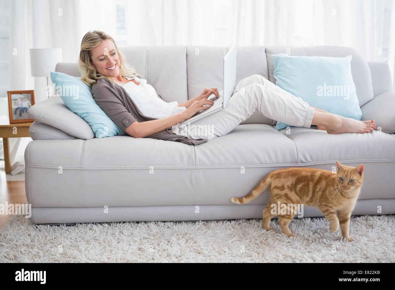 Pretty woman lying on sofa using her laptop Stock Photo - Alamy