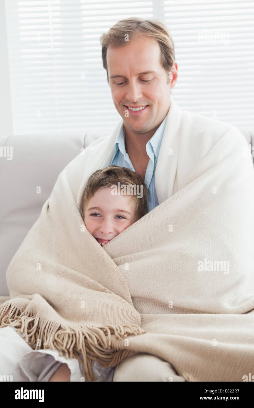 Father and son wrapped in a blanket on the couch Stock Photo Alamy