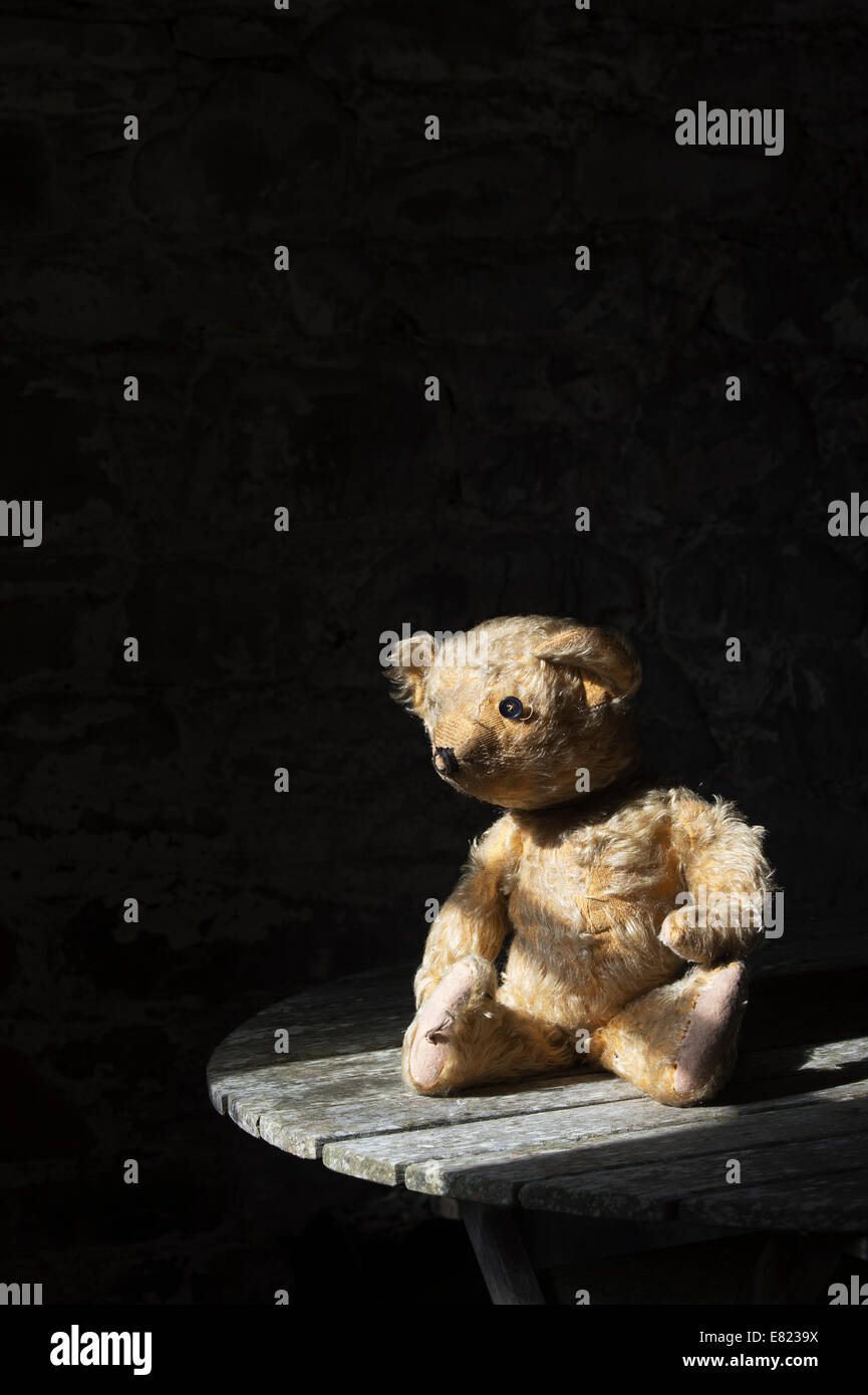 Old Threadbare One Eyed Teddy bear sat on a wooden table in sunlight Stock Photo