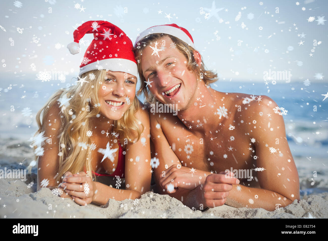 Composite image of couple lying on beach wearing christmas hats Stock Photo