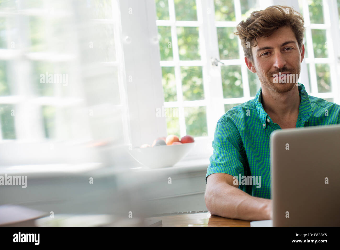 A man seated at a table using a laptop. Working from home. Stock Photo