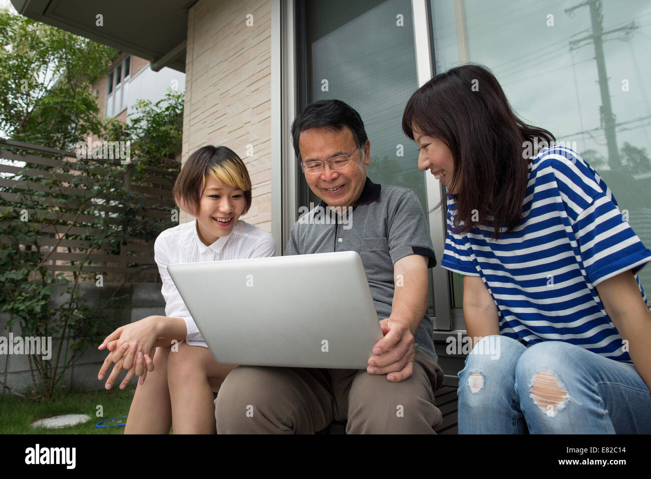A man and two women sitting outside a house. Holding a laptop computer. Stock Photo