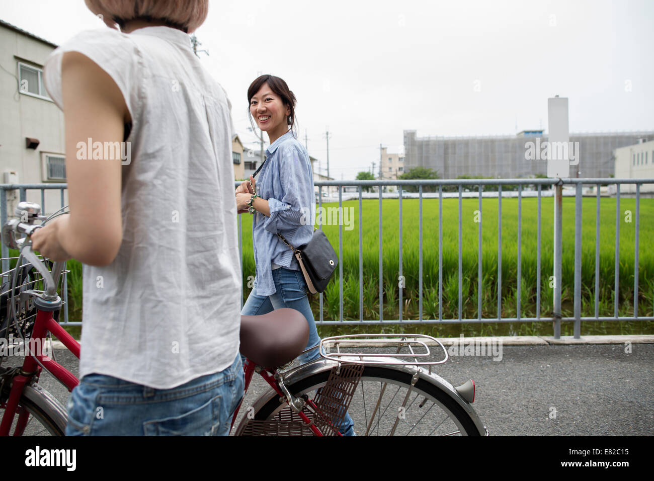 Two women walking along a footpath, pushing a bicycle. Stock Photo