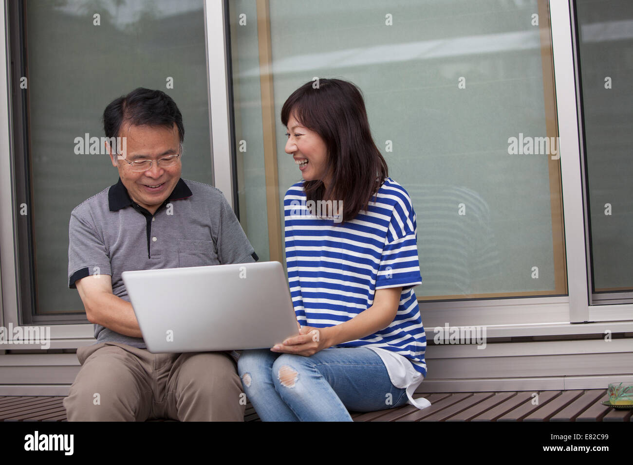 A man and a women sitting outside a house. Holding a laptop computer. Stock Photo