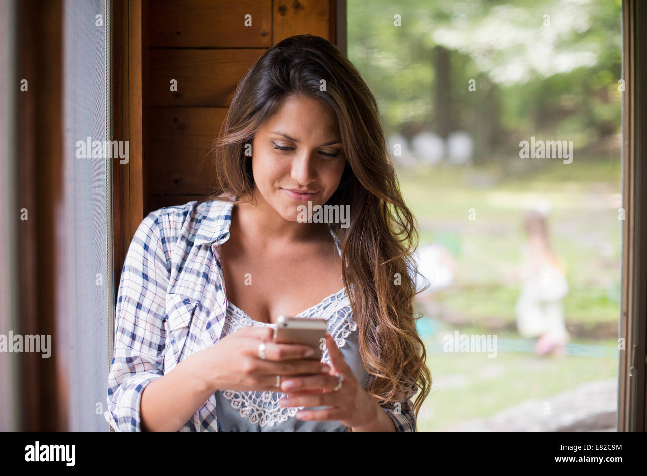 A woman sitting by a window, looking at her cell phone. Stock Photo
