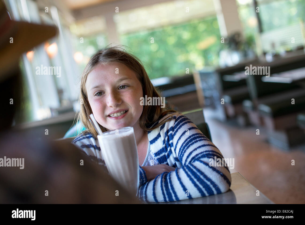 A young girl with a large milk shake at a diner table. Stock Photo
