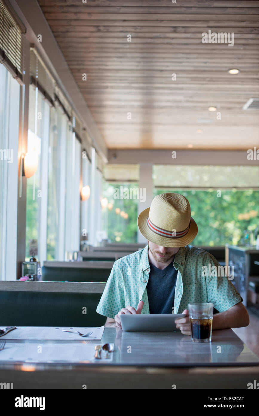 A man wearing a hat sitting in a diner using a digital tablet. Stock Photo
