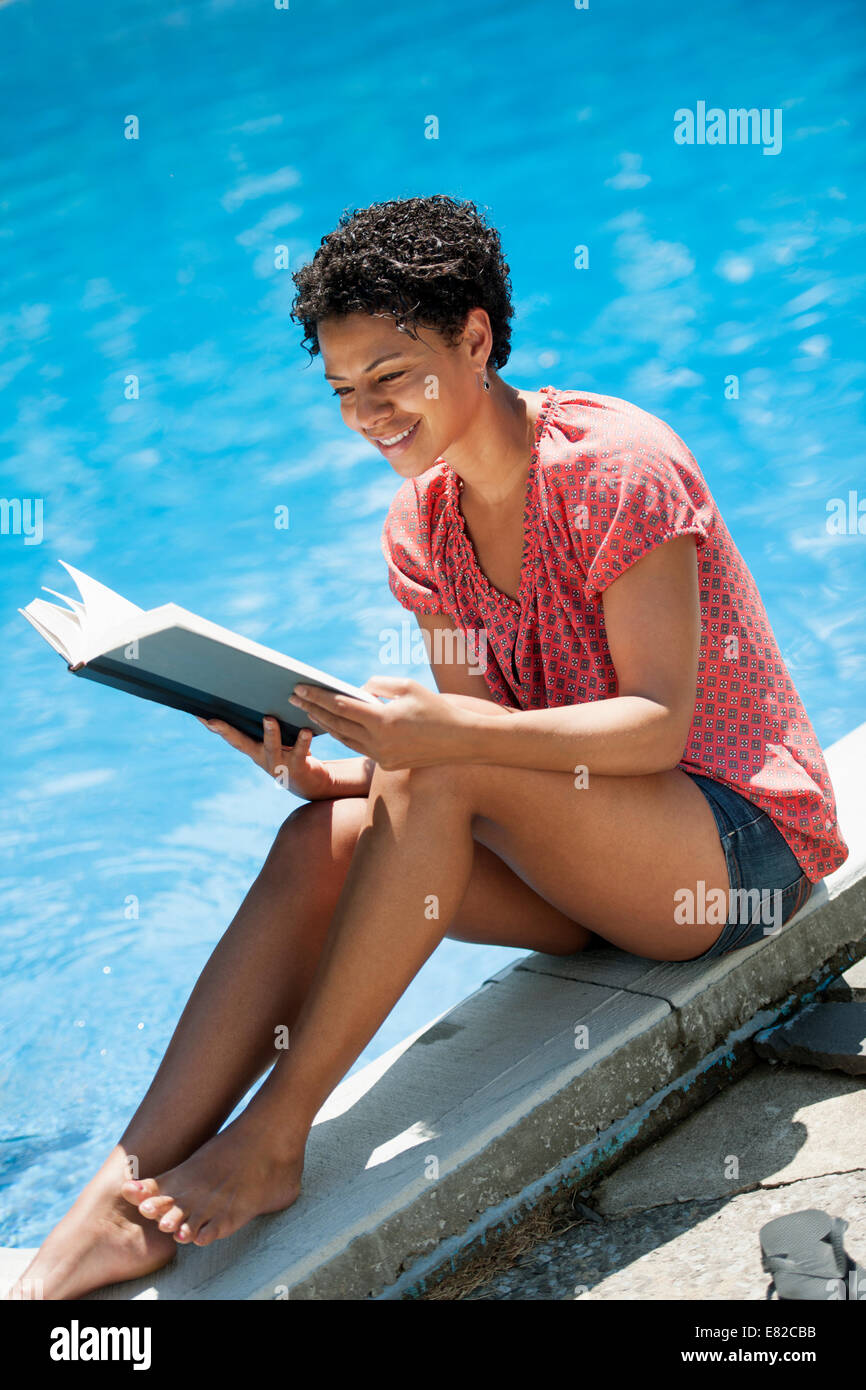 A woman sitting at a swimming pool, reading a book Stock Photo - Alamy