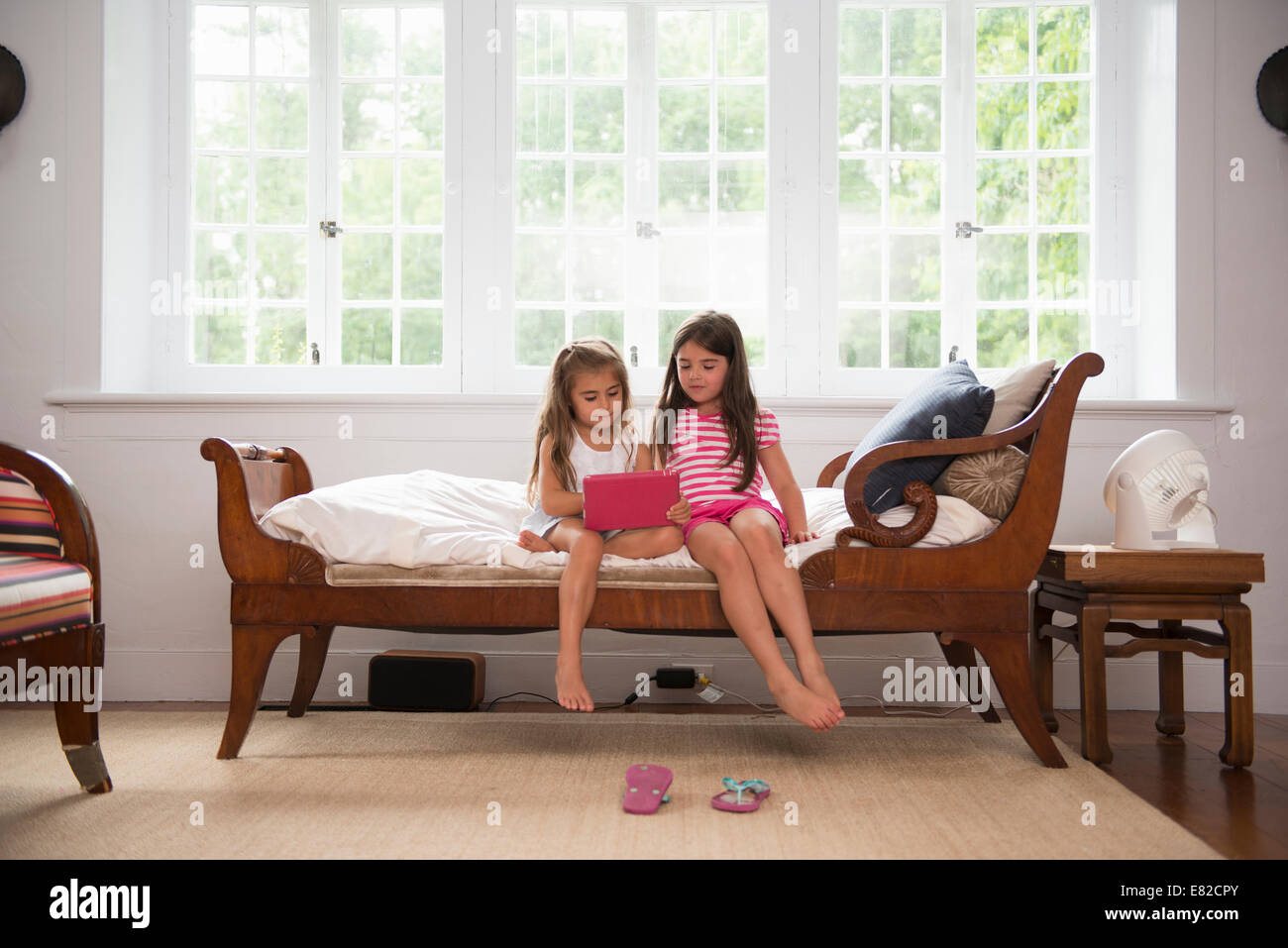 Two girls playing indoors, looking at a digital tablet. Stock Photo