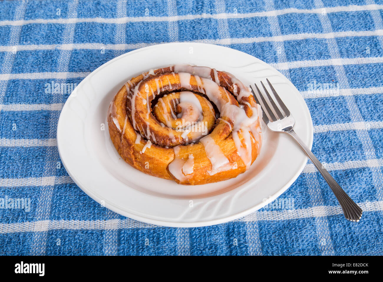 A fresh cinnamon roll on a white plate with fork Stock Photo - Alamy