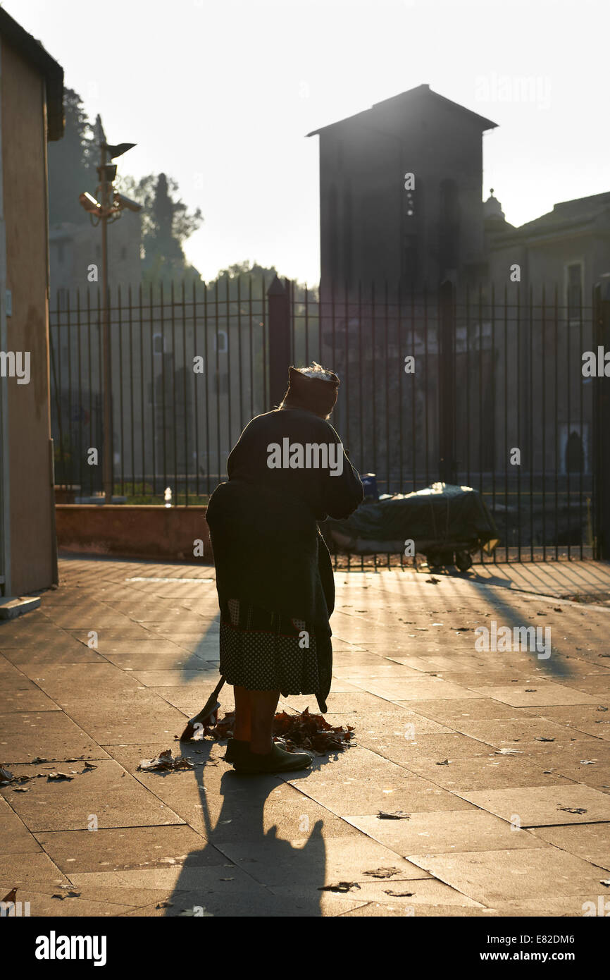 Old woman sweeping the sidewalk in the morning sun in Rome, Italy Stock Photo