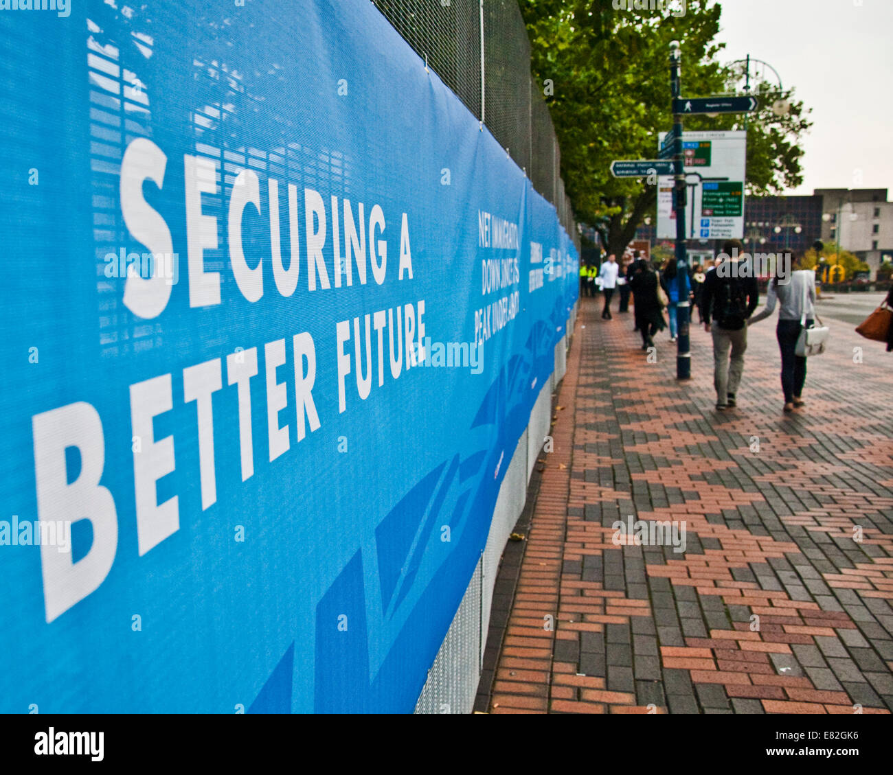 Birmingham, UK 29//2014. A couple walk past a Conservative slogan declaring that the party will secure a better future at its annual conference in Birmingham (C) Paul Swinney/Alamy Live News Stock Photo