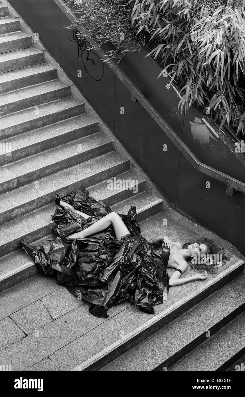 Woman wearing dress made from bin bags lying on stairs Stock Photo